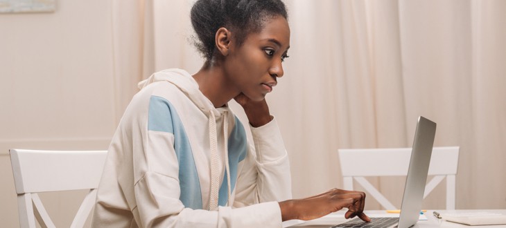 Female student working on laptop computer while sitting on white chair at white table